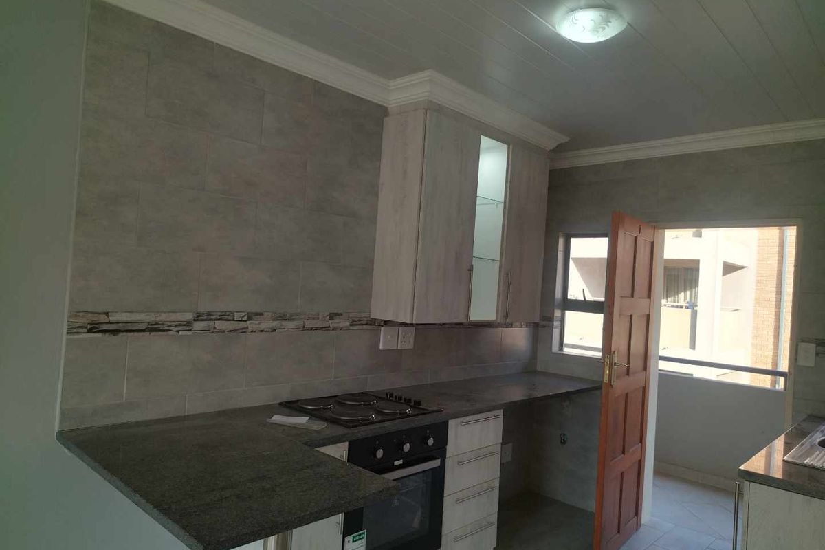 Modern kitchen featuring stone-look countertops, built-in oven and hob, tiled backsplash, and light wood cabinetry with direct access to a balcony.