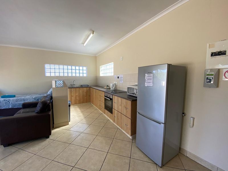 Open-plan kitchen area featuring wood-finish cabinetry, laminate countertops, built-in oven, hob, and glass block windows with ceramic tiled flooring.