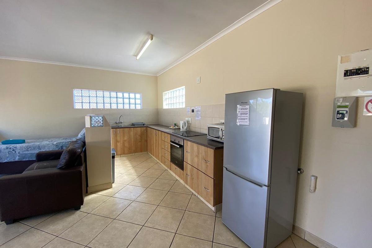 Open-plan kitchen area featuring wood-finish cabinetry, laminate countertops, built-in oven, hob, and glass block windows with ceramic tiled flooring.