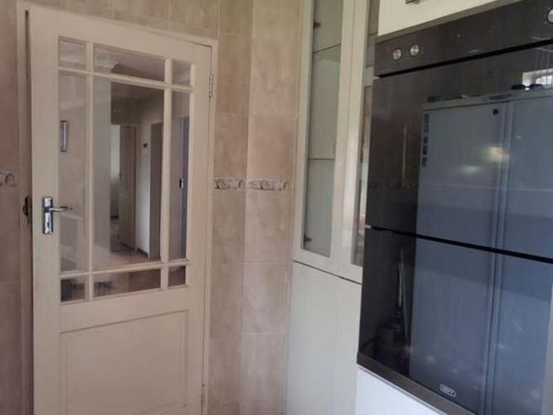 A functional kitchen area featuring built-in oven cabinetry, tiled walls, and flooring, with a classic glass-panelled door leading to the hallway.