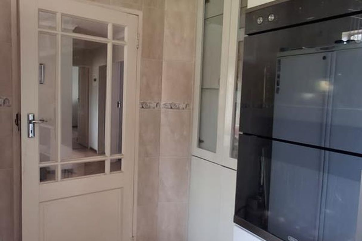 A functional kitchen area featuring built-in oven cabinetry, tiled walls, and flooring, with a classic glass-panelled door leading to the hallway.