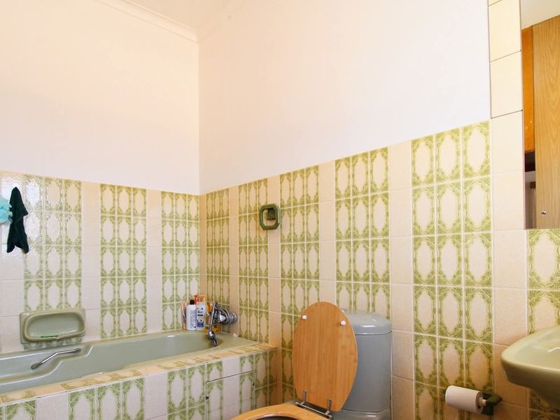 A dated bathroom featuring vintage green sanitaryware, a built-in bathtub, and patterned wall tiles, offering significant potential for a modern renovation.