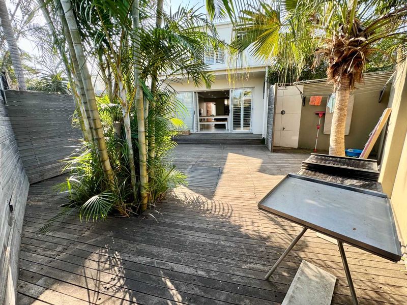 Rear courtyard featuring timber decking, established palm trees, and direct access to the interior living space through sliding glass doors.