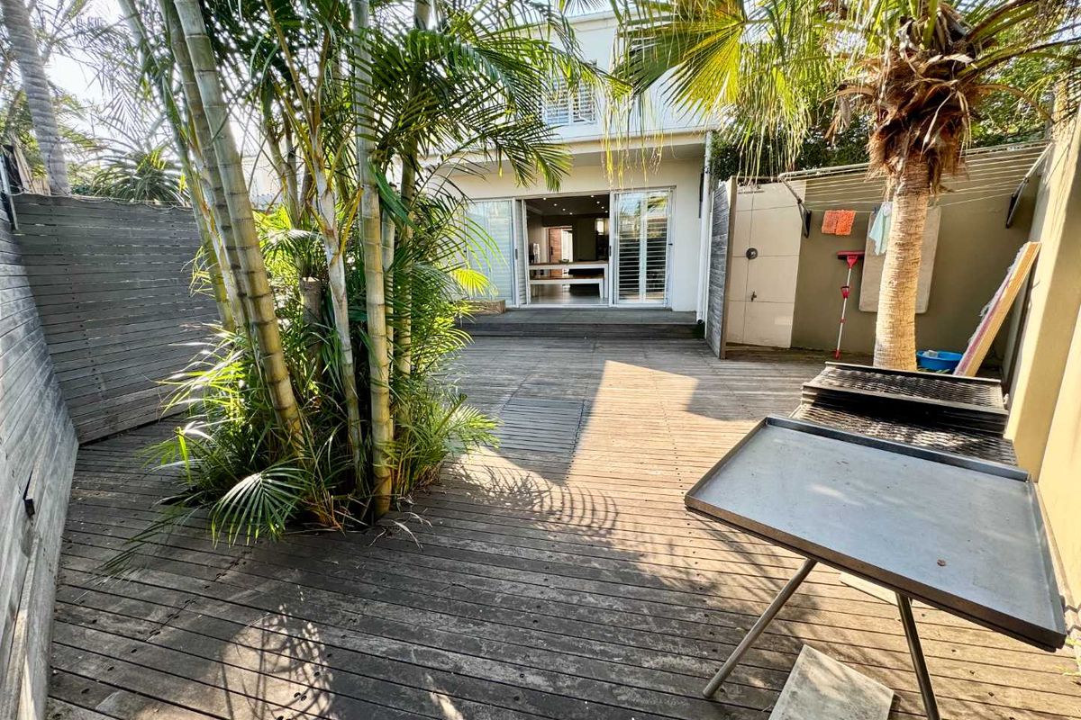 Rear courtyard featuring timber decking, established palm trees, and direct access to the interior living space through sliding glass doors.