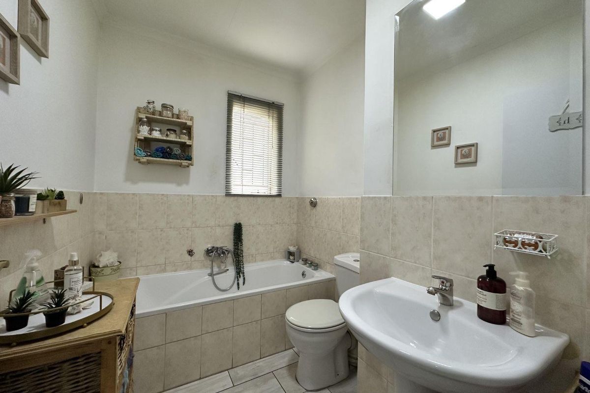 A functional bathroom featuring a built-in bathtub, pedestal sink, toilet, and wall-mounted mirror with neutral tiled finishes.