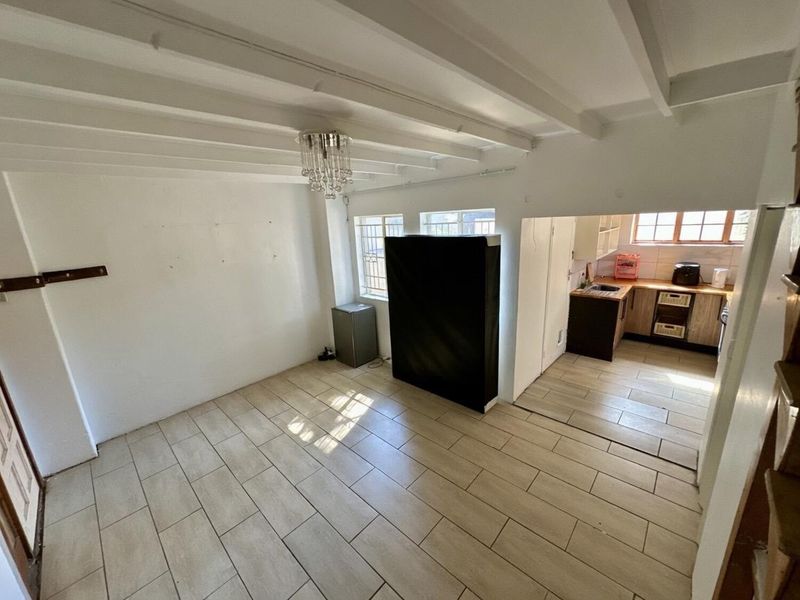 Open plan living area featuring tiled floors and exposed beam ceilings, seamlessly connected to a functional kitchen with wooden countertops and cabinetry.