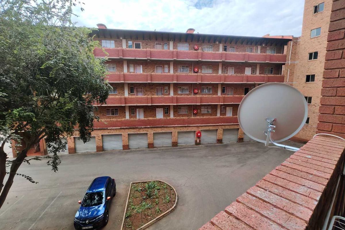 View of the apartment complex exterior featuring multi-level brick facade, ground-level garage units, and paved courtyard area.
