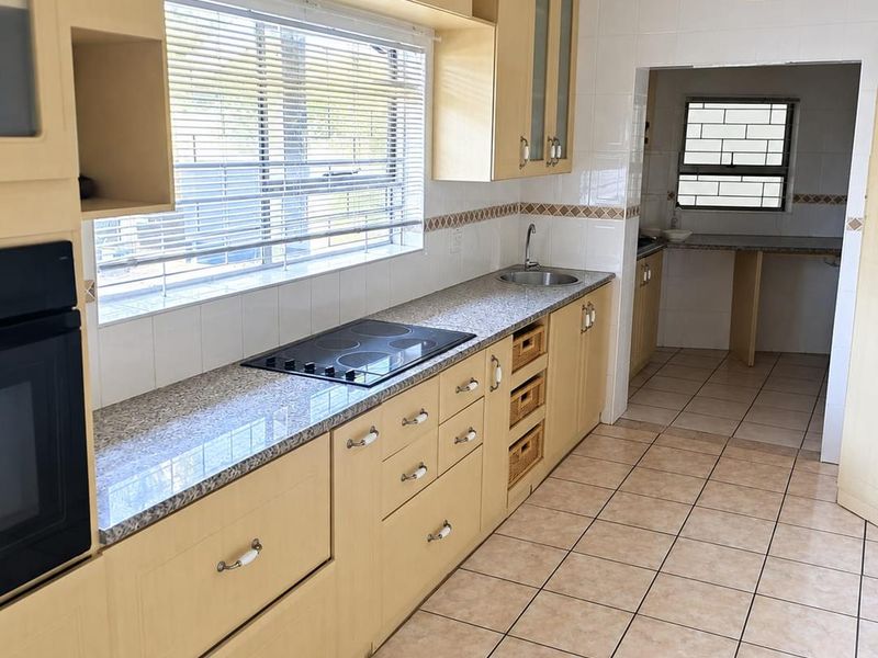 A functional kitchen featuring light wood cabinetry, granite countertops, a built-in oven, and an electric hob, with an adjacent scullery area.