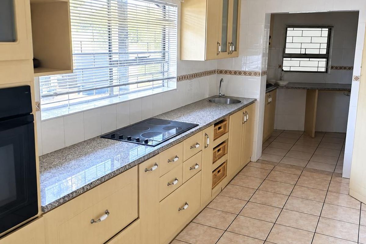 A functional kitchen featuring light wood cabinetry, granite countertops, a built-in oven, and an electric hob, with an adjacent scullery area.