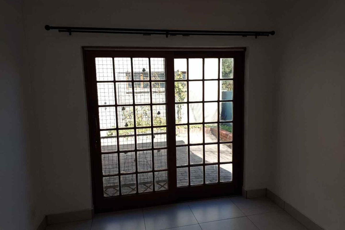 An empty room featuring tiled flooring and wooden sliding doors that open onto a paved outdoor area.