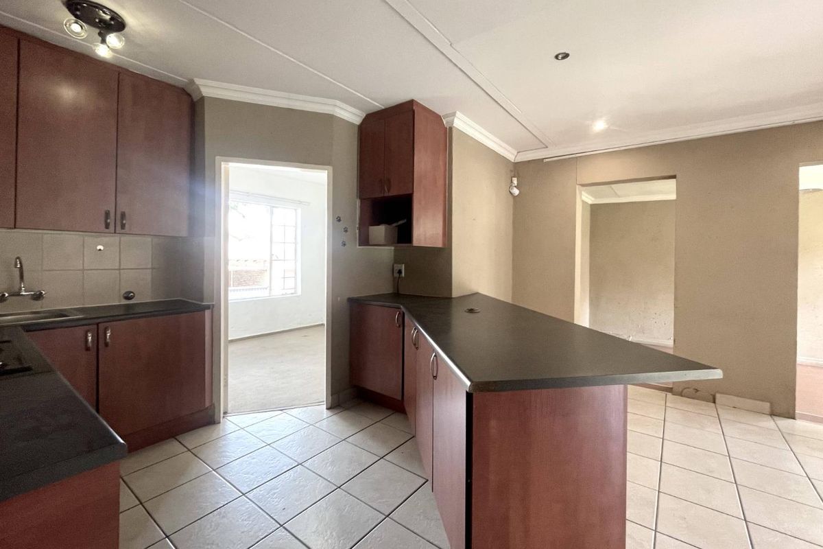 A functional kitchen featuring dark wood-look cabinetry, dark laminate countertops, tiled flooring, and a breakfast bar peninsula, connecting to adjacent living spaces.