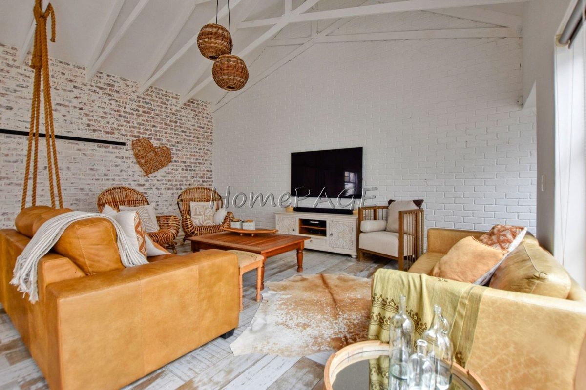 Spacious living room featuring a vaulted ceiling with exposed beams and a distinctive white-painted brick feature wall.