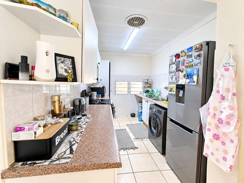 A functional kitchen featuring laminate countertops, tiled backsplash, ceramic flooring, and built-in cabinetry with integrated sink and appliance space.
