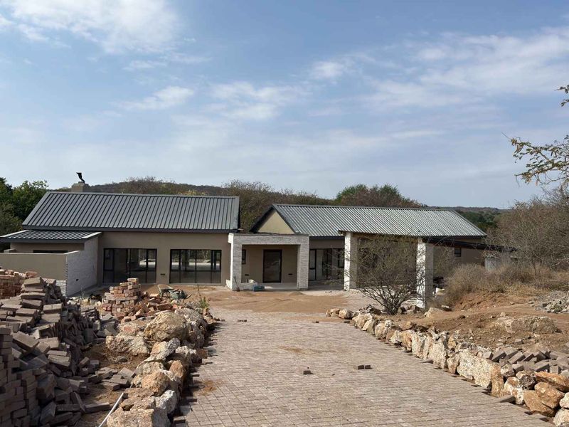 A modern single-story house featuring a metal roof, stone accents, and a paved driveway, currently undergoing final exterior landscaping and site completion.