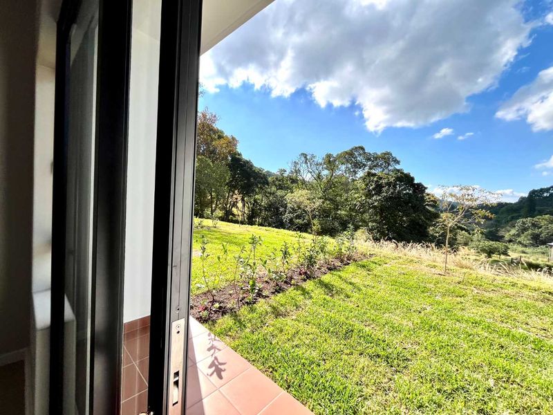 A view from a tiled patio looking out over a lush green lawn and surrounding trees under a bright blue sky.