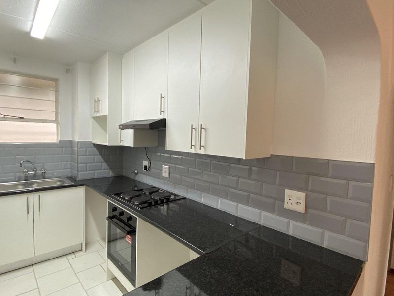 A clean, modern kitchen featuring white cabinetry, black granite countertops, subway tile backsplash, and integrated stainless steel appliances.