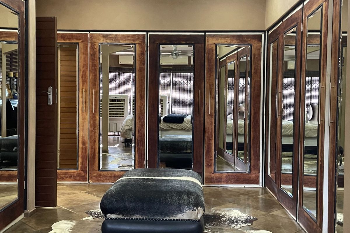 A spacious dressing room featuring extensive floor-to-ceiling built-in wooden cupboards with integrated mirror panels and tiled flooring.