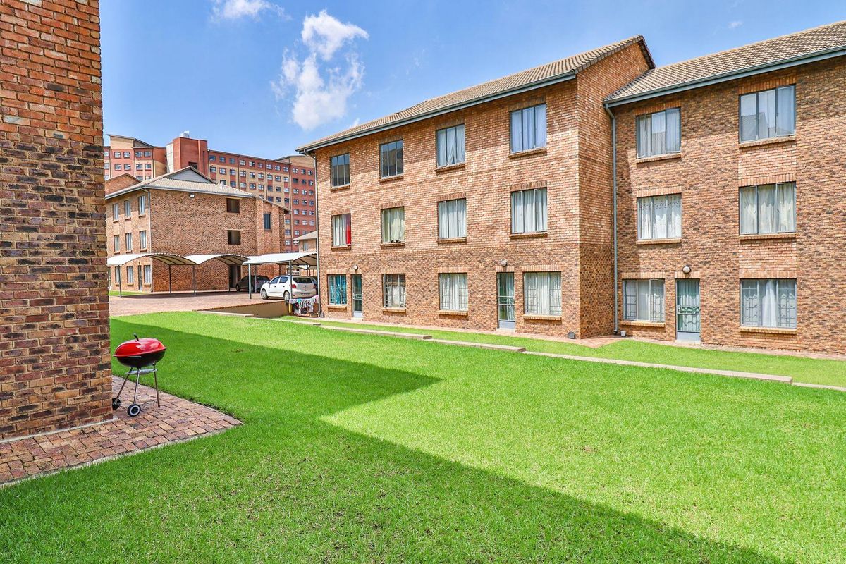 Exterior view of a multi-story brick apartment complex featuring a well-maintained communal lawn area and covered parking bays.