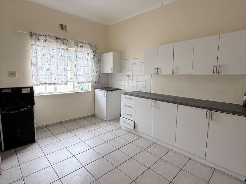 A functional kitchen featuring white cabinetry, tiled flooring, and a tiled backsplash, offering a clean canvas for potential modern updates.