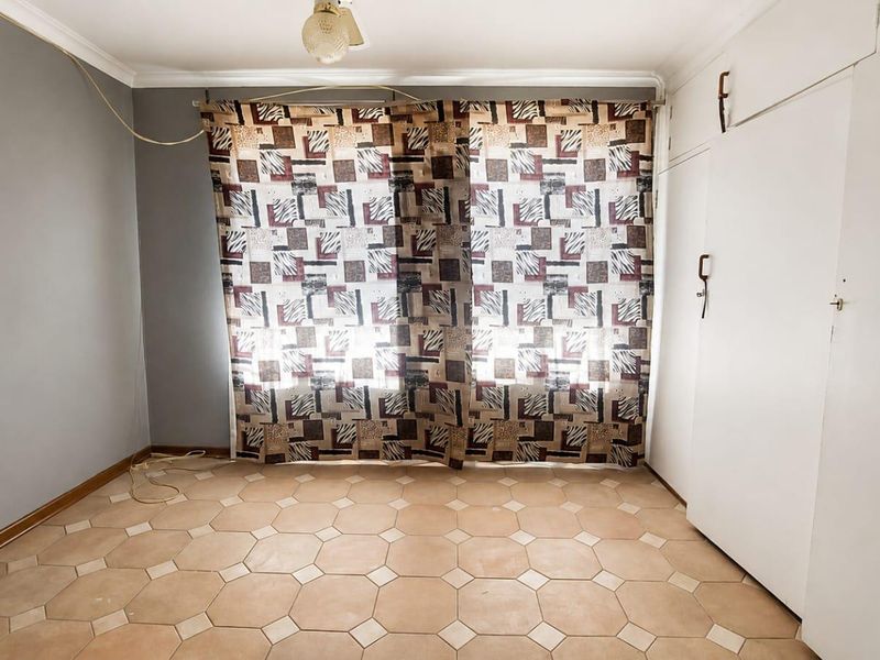 An empty bedroom featuring built-in cupboards, tiled flooring, and neutral wall finishes, offering a blank canvas for potential updates.