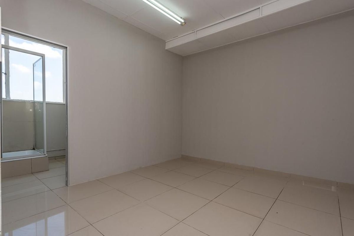 An empty bedroom featuring neutral tiled flooring, plain walls, and a doorway leading to an adjacent balcony area.