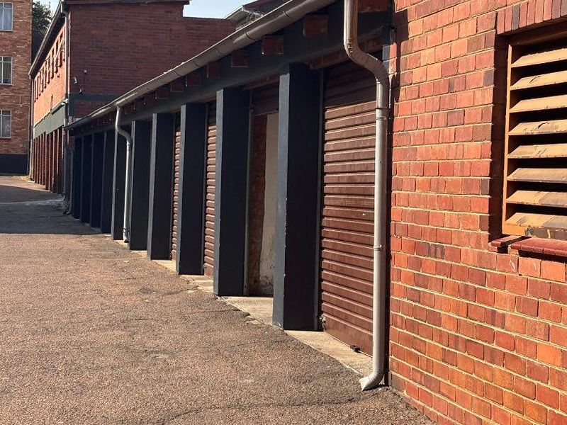 A row of brick-built garages featuring roller shutter doors, external guttering, and downpipes, situated along an asphalt driveway.