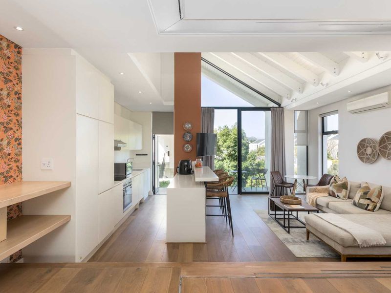 Modern open-plan living area featuring a sleek kitchen with integrated appliances, vaulted ceilings with exposed beams, and seamless access to a private balcony.