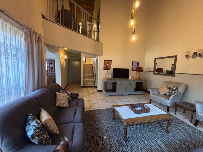 Spacious double-volume living room featuring tiled floors, a mezzanine balcony with metal balustrade, and a staircase leading to the upper level.