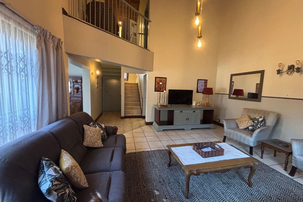 Spacious double-volume living room featuring tiled floors, a mezzanine balcony with metal balustrade, and a staircase leading to the upper level.
