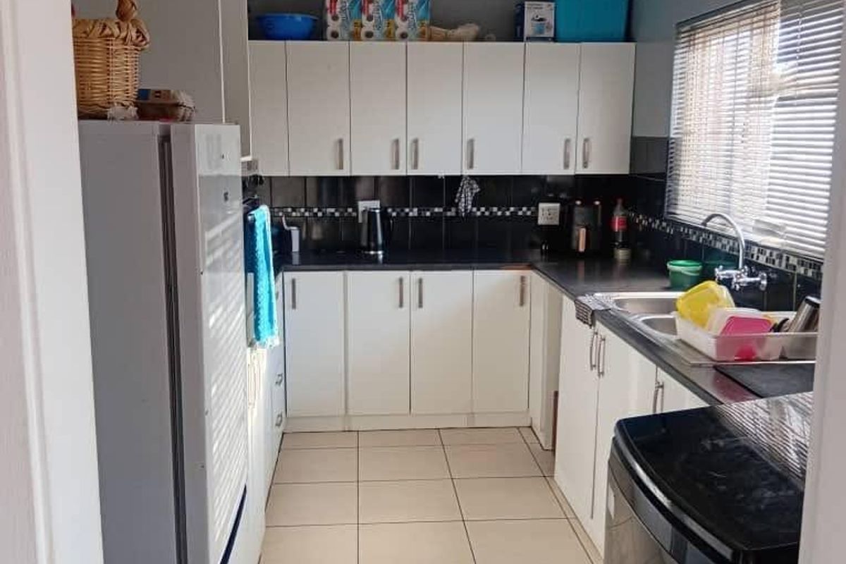A functional galley-style kitchen featuring white cabinetry, dark countertops, tiled backsplash, and ceramic floor tiles with a window for natural light.
