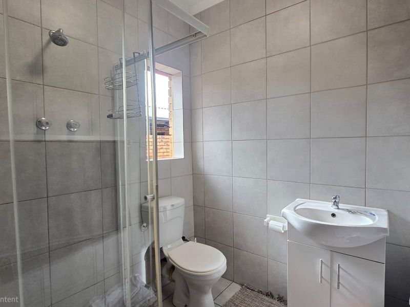 A modern bathroom featuring a glass-enclosed shower, a white vanity with a basin, and neutral wall tiling.