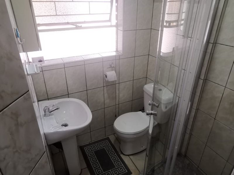 Compact bathroom featuring a pedestal basin, toilet, and a glass-enclosed shower with full-height wall tiling.