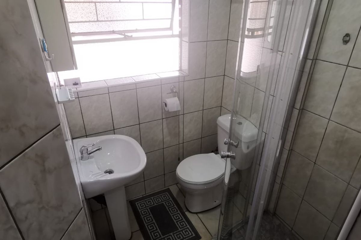 Compact bathroom featuring a pedestal basin, toilet, and a glass-enclosed shower with full-height wall tiling.