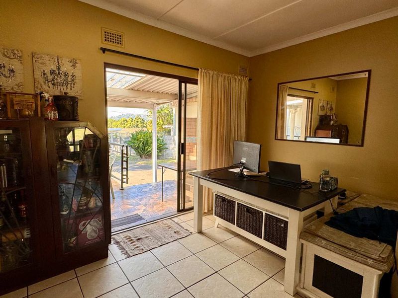 A functional home office space featuring ceramic floor tiles and a sliding glass door providing direct access to an outdoor patio area.