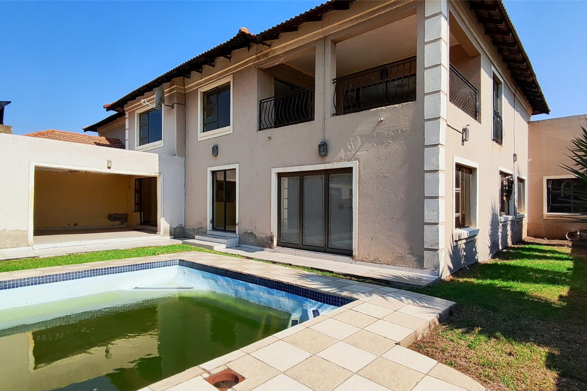 Rear view of a two-story house featuring a covered patio, upper-level balcony, and a swimming pool requiring maintenance.