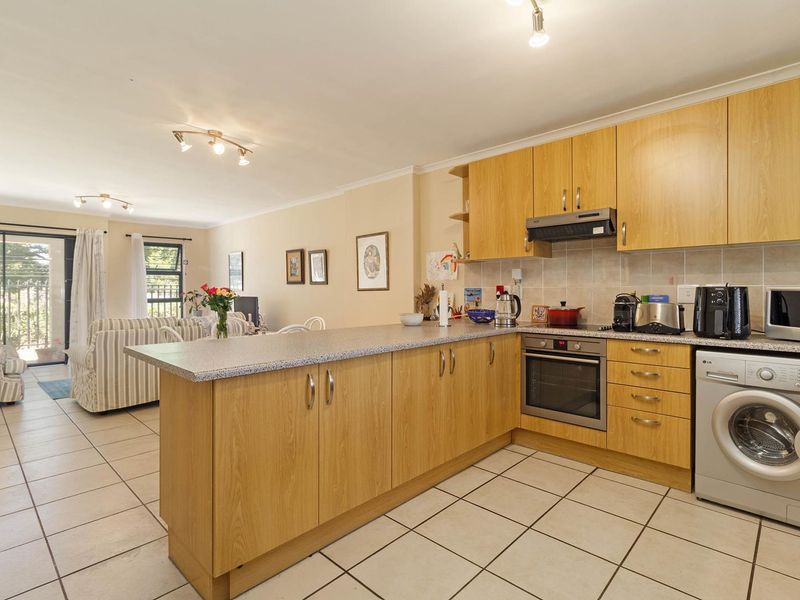 Open-plan kitchen and living area featuring light wood cabinetry, granite countertops, tiled flooring, and direct access to a patio through sliding glass doors.