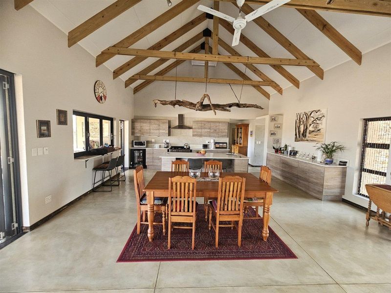 Spacious open-plan living and dining area featuring high vaulted ceilings with exposed timber trusses, polished concrete floors, and a modern kitchen with a central island.