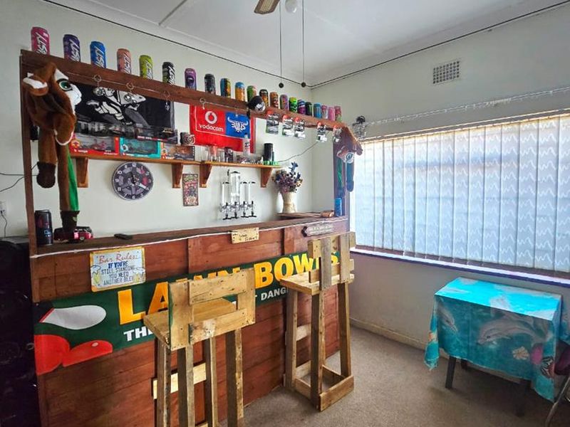 A dedicated bar area featuring a built-in wooden counter, ceiling fan, and large window with vertical blinds, offering potential for a modern entertainment space.