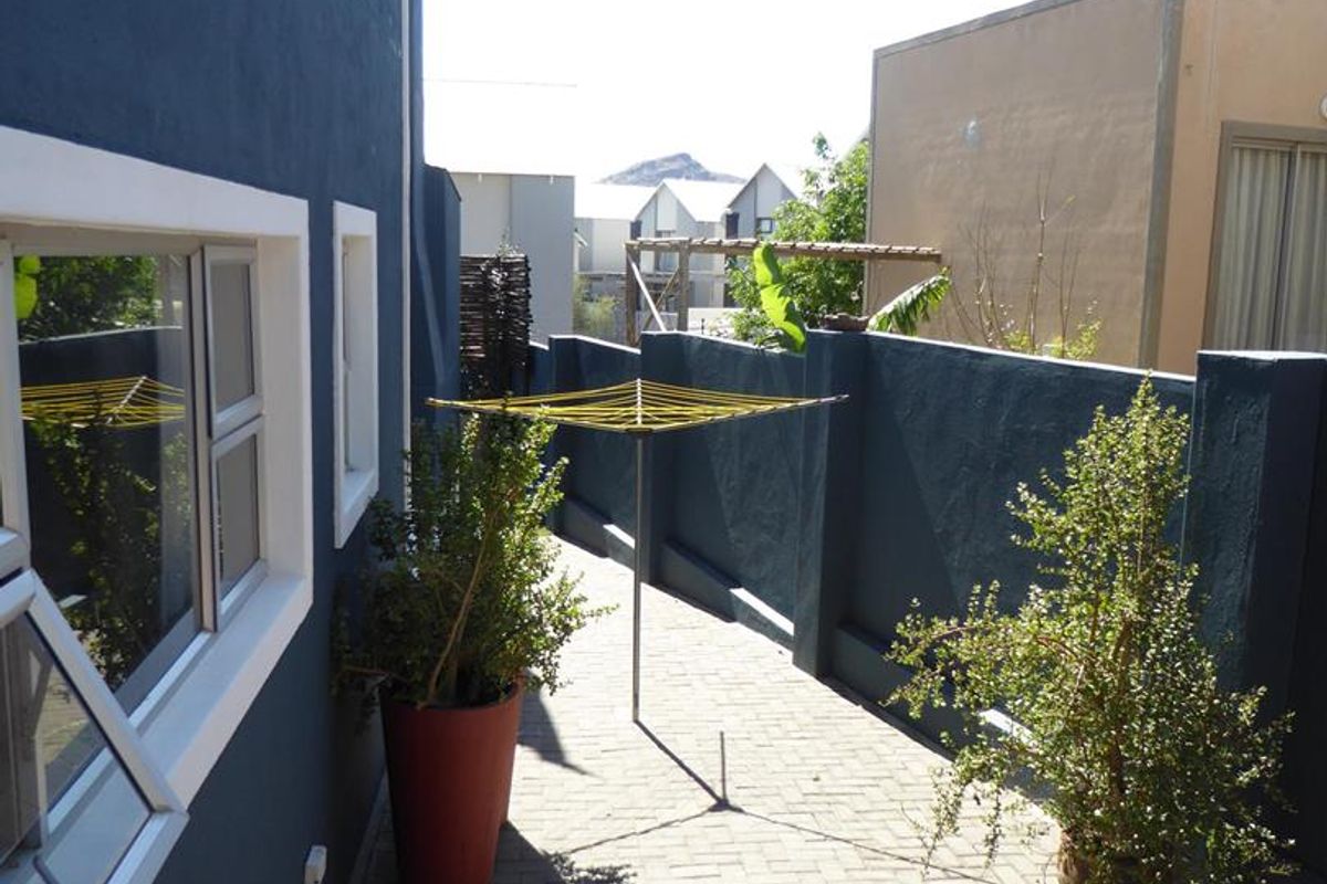 A paved side walkway or rear courtyard area featuring dark painted boundary walls and aluminium window frames.