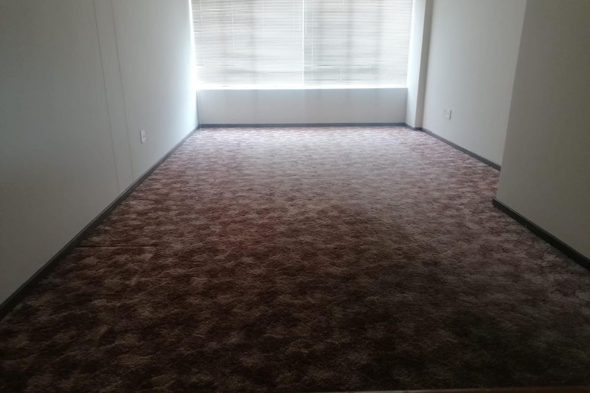 An empty bedroom featuring wall-to-wall carpeting and large windows with fitted blinds, offering a blank canvas for personalization.