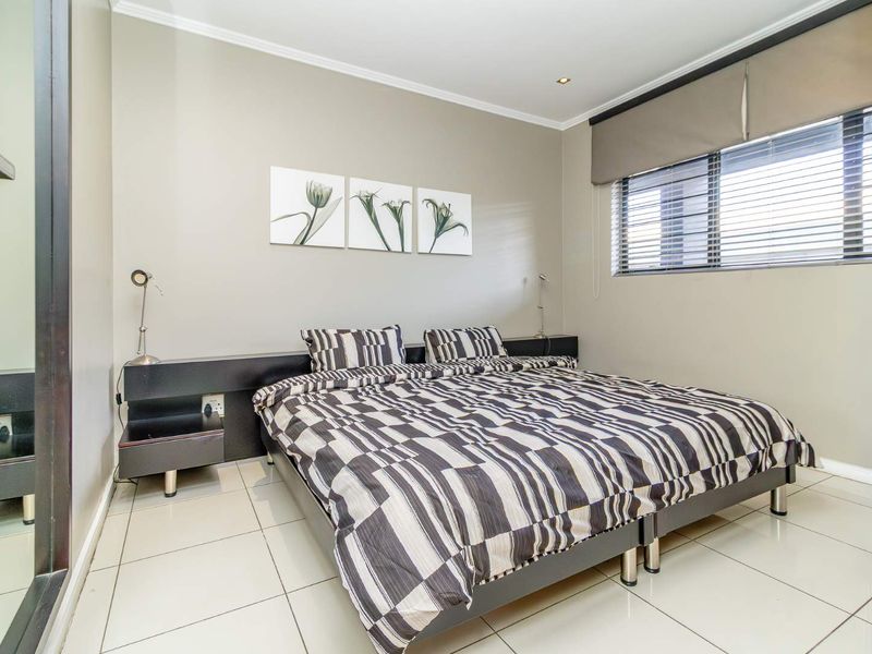 A well-maintained bedroom featuring neutral wall tones, tiled flooring, recessed lighting, and a functional built-in headboard with integrated electrical points.