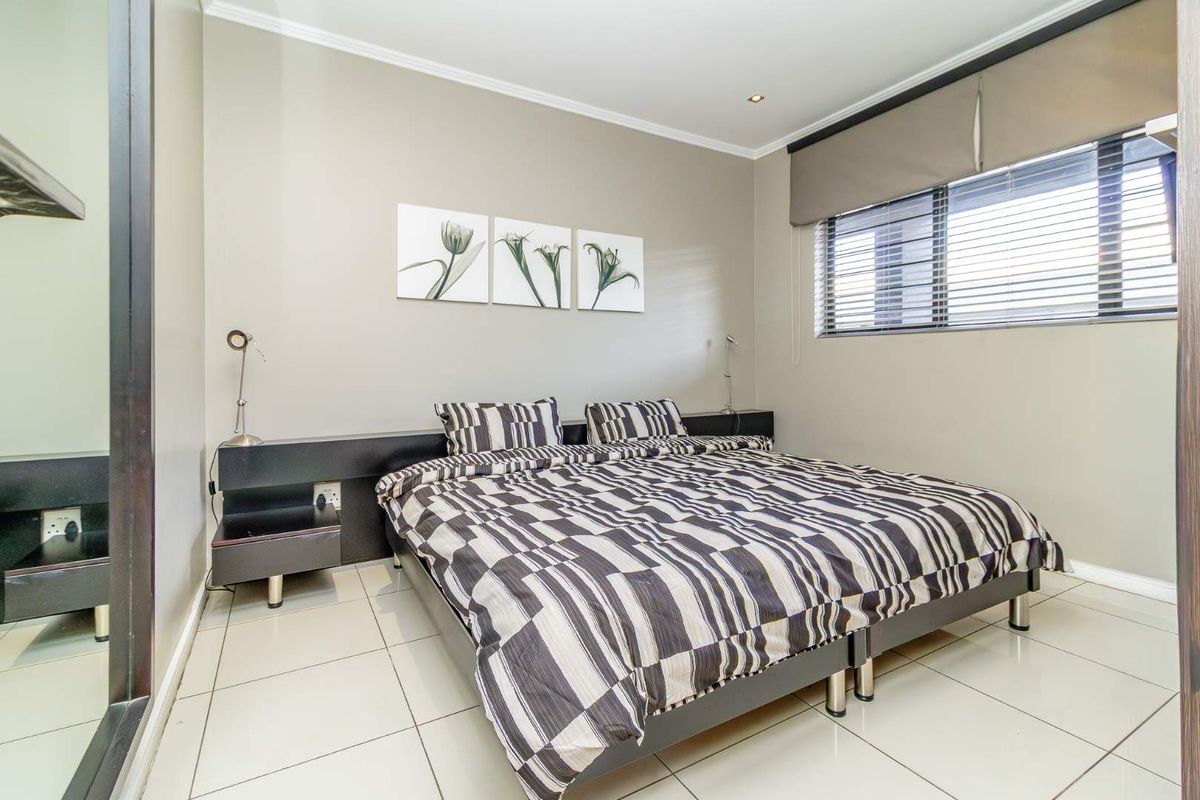 A well-maintained bedroom featuring neutral wall tones, tiled flooring, recessed lighting, and a functional built-in headboard with integrated electrical points.