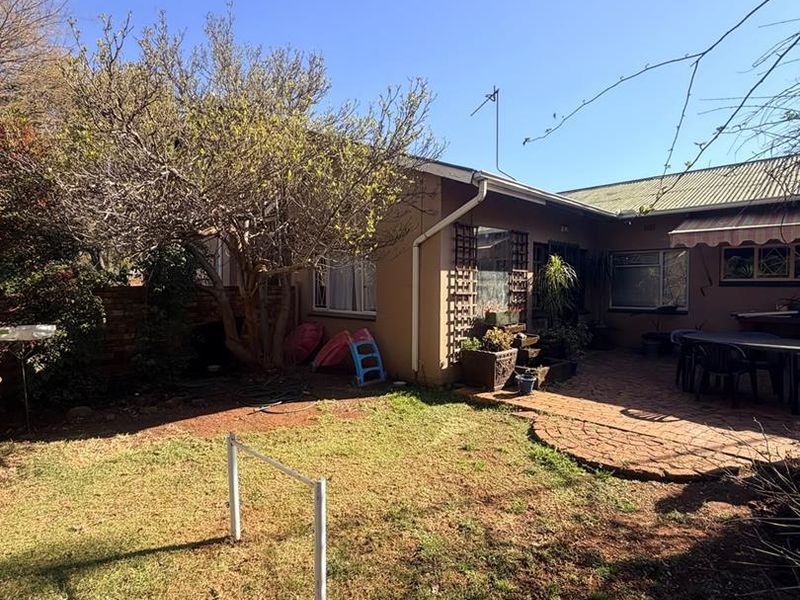 Rear view of the property featuring a brick paved patio area, established garden, and metal roof structure.