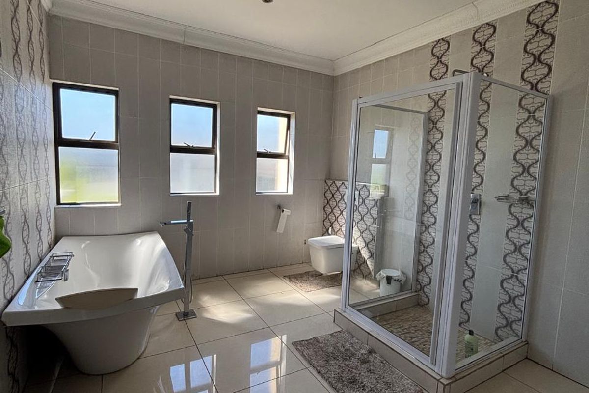 Spacious modern bathroom featuring a freestanding bathtub, glass-enclosed shower, wall-mounted toilet, and neutral floor-to-ceiling tiling with decorative accents.