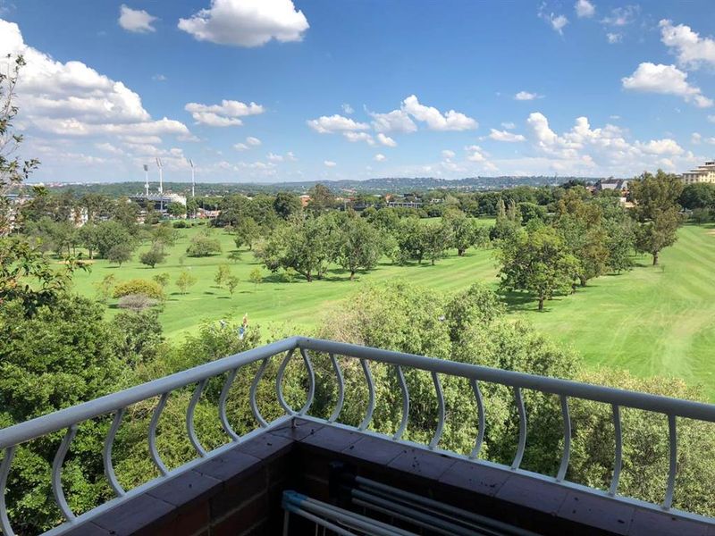 A scenic elevated view overlooking a lush green golf course and surrounding landscape, captured from a private balcony with a metal railing.