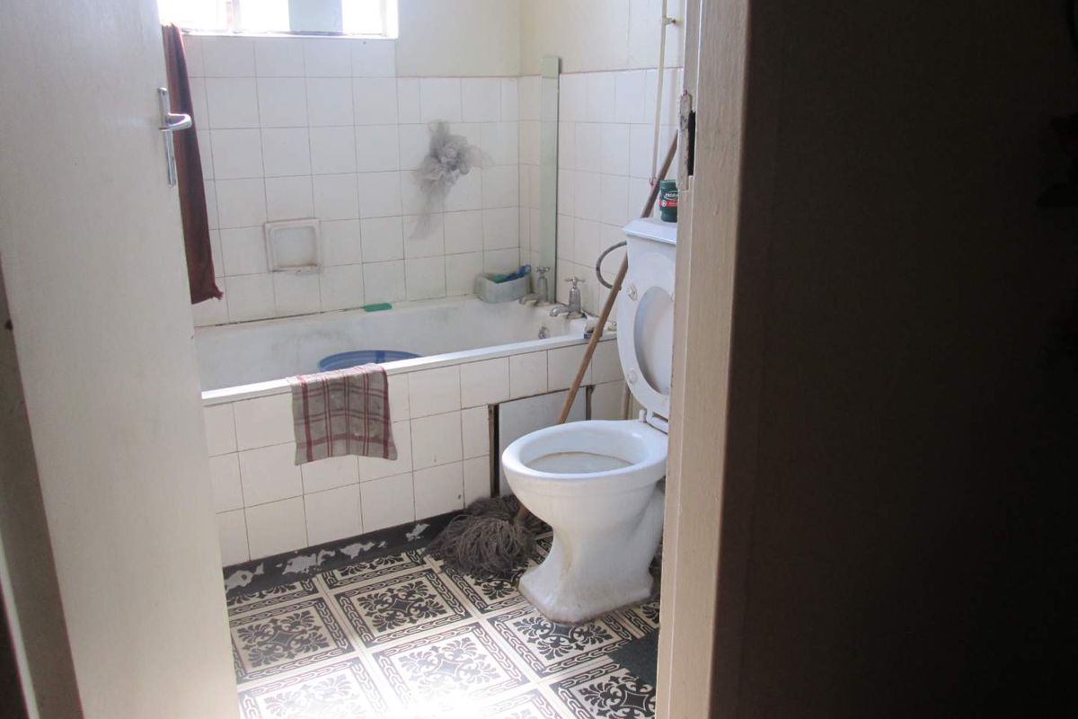 A dated bathroom featuring a standard bathtub, toilet, and patterned floor tiles. The space requires renovation to update finishes and improve overall condition.