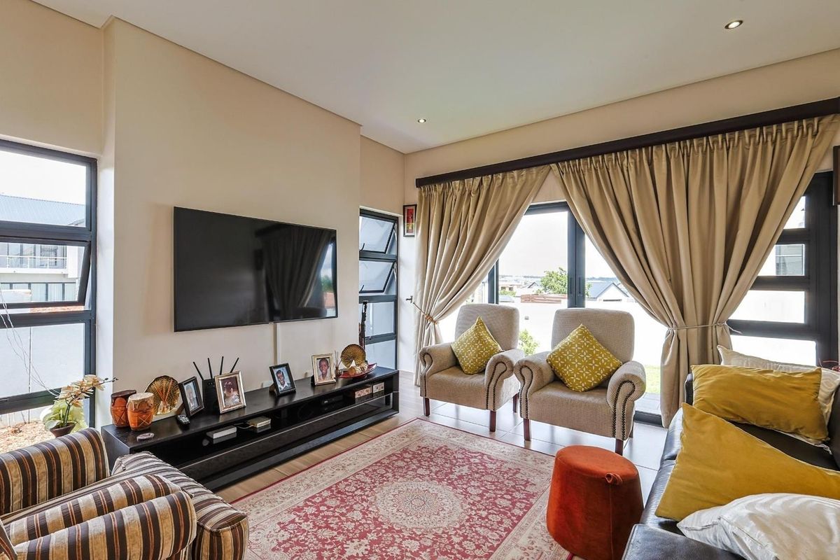 A bright and comfortable living room featuring large windows, tiled flooring, and recessed ceiling lighting, offering a pleasant space for relaxation.