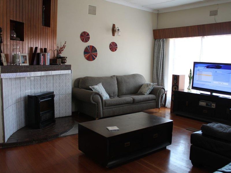 A living room featuring timber flooring, a fireplace with decorative tiling, and timber wall paneling accents.