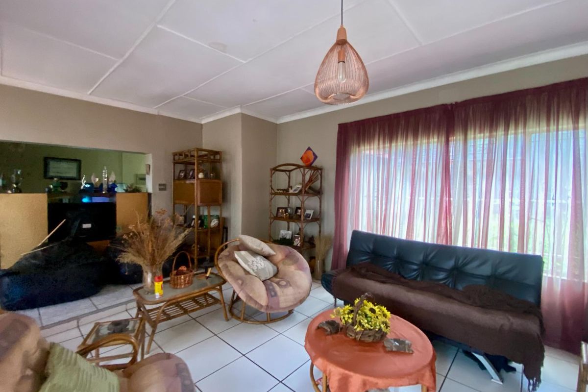 A living room featuring white tiled flooring, a suspended pendant light fixture, and large windows with sheer curtains, offering a functional living space.