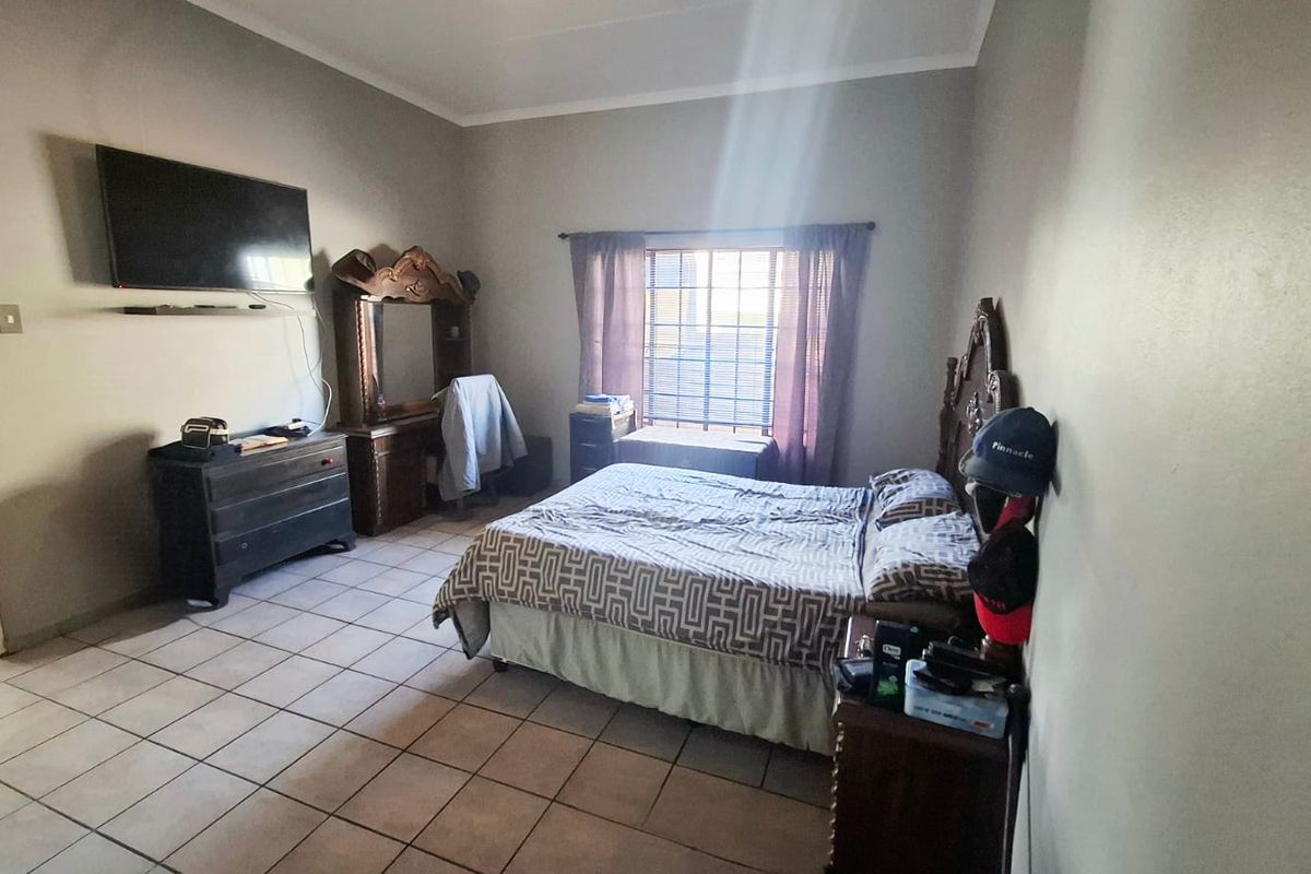 A functional bedroom featuring tiled flooring, neutral wall tones, and a window fitted with security bars.